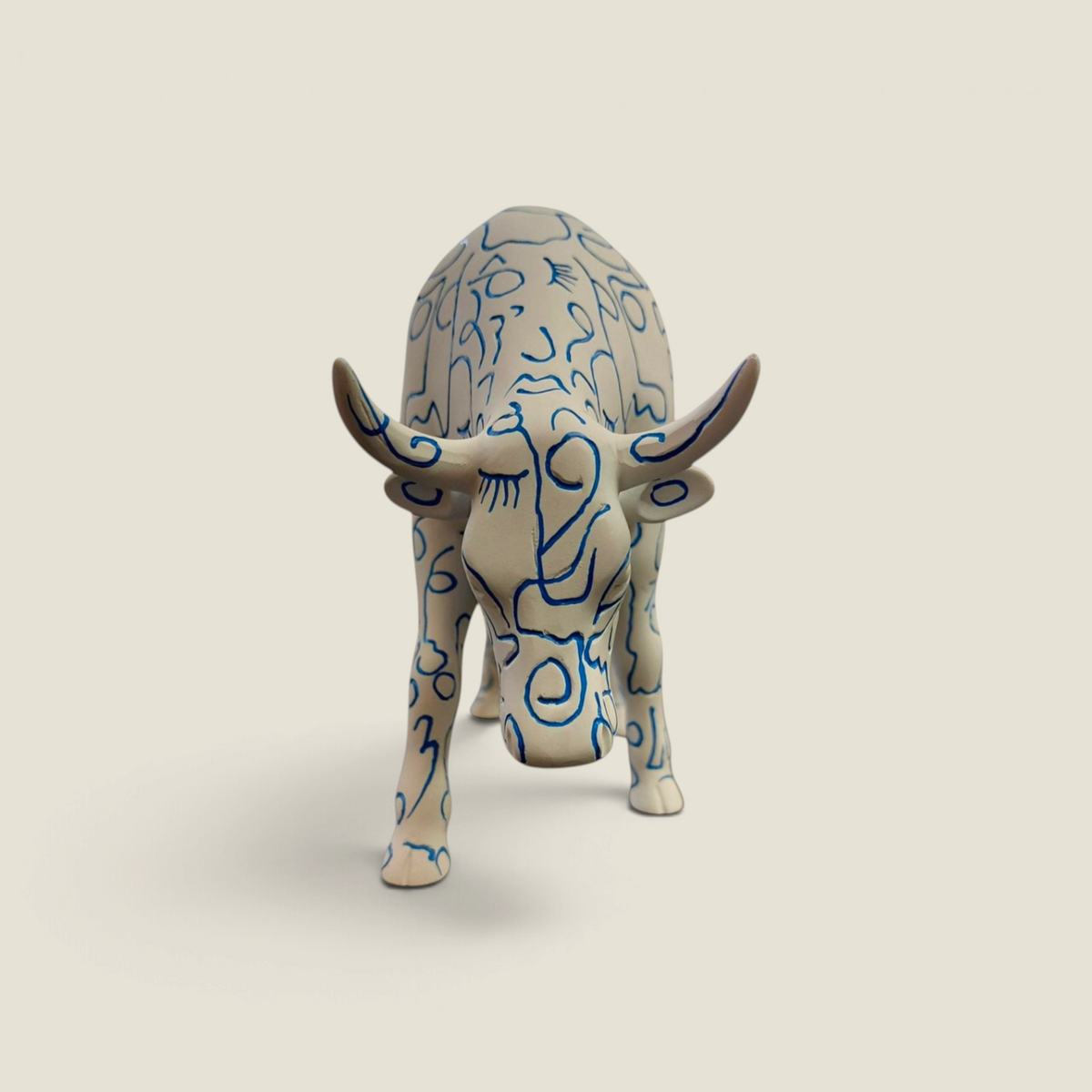 Figurine vache en résine Depuis des lustres, peinte à la main avec des motifs de visages bleus sur fond blanc.
