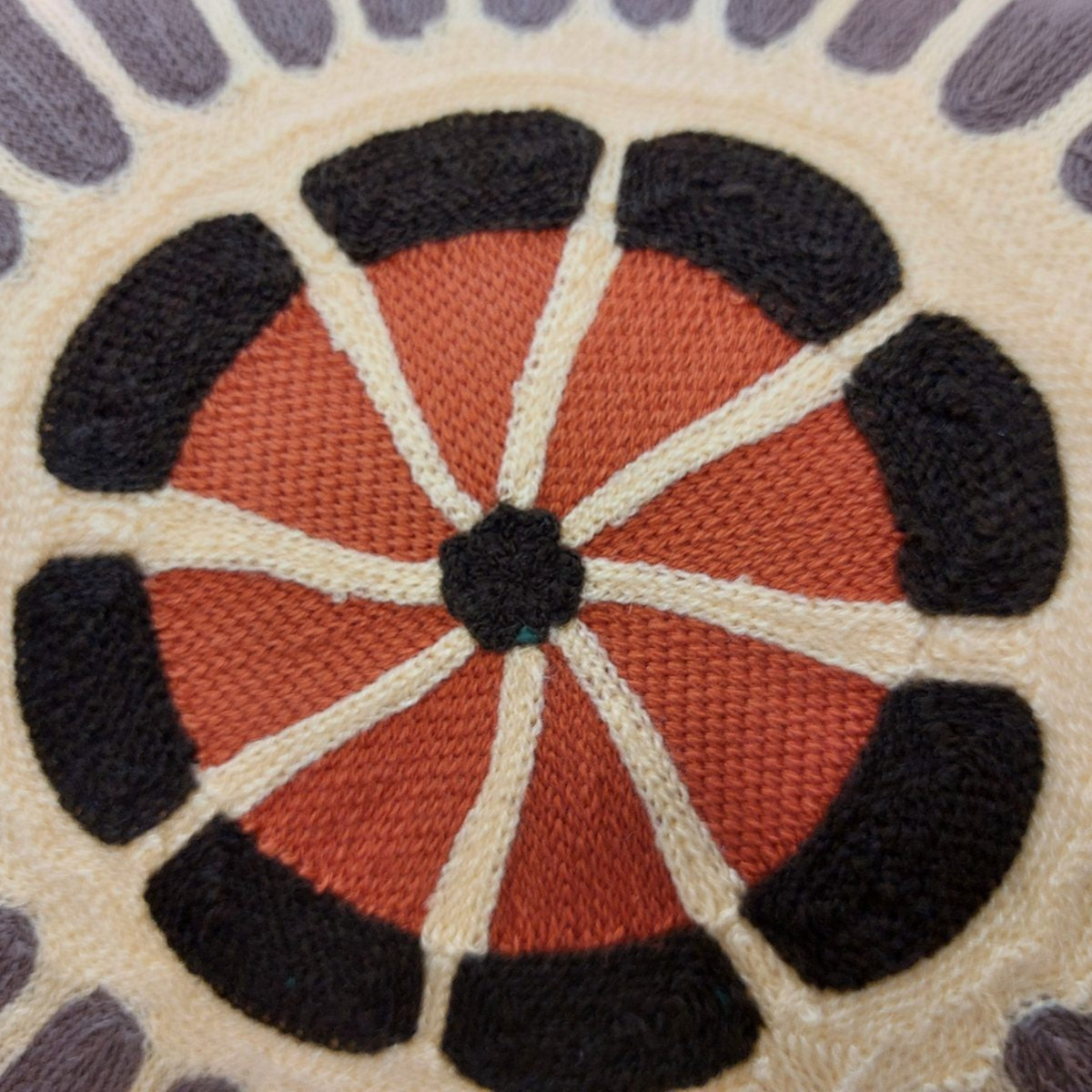 Gros plan sur la broderie artisanale du coussin Depuis des lustres Zeno Forêt aux motifs géométriques colorés