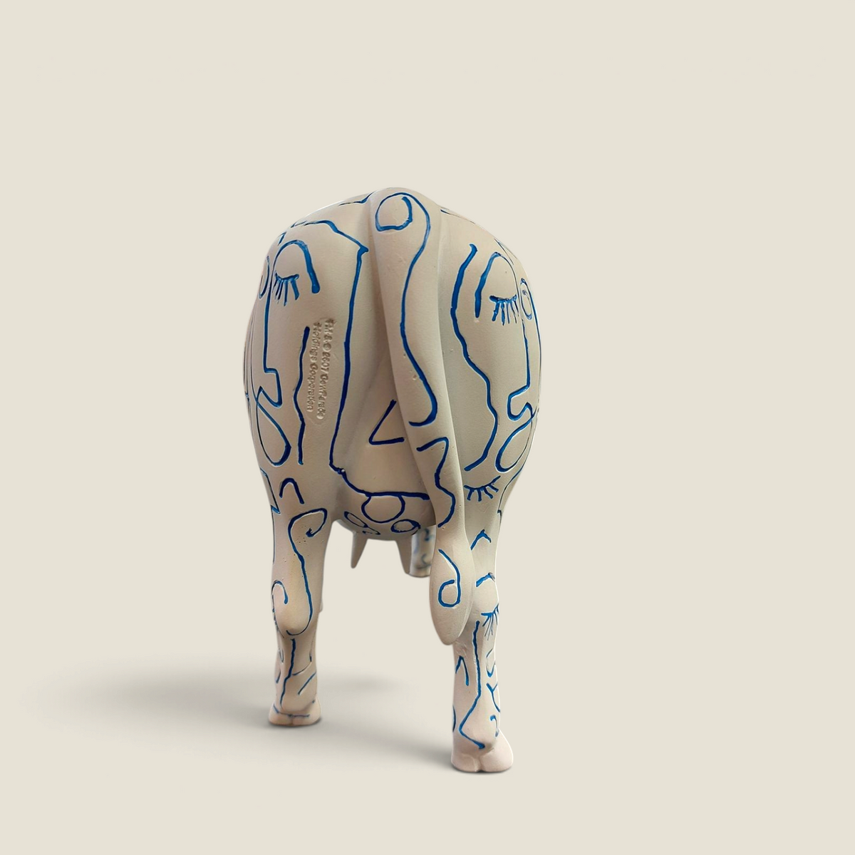 Figurine vache en résine Depuis des lustres, peinte à la main avec des visages bleus stylisés sur fond blanc.
