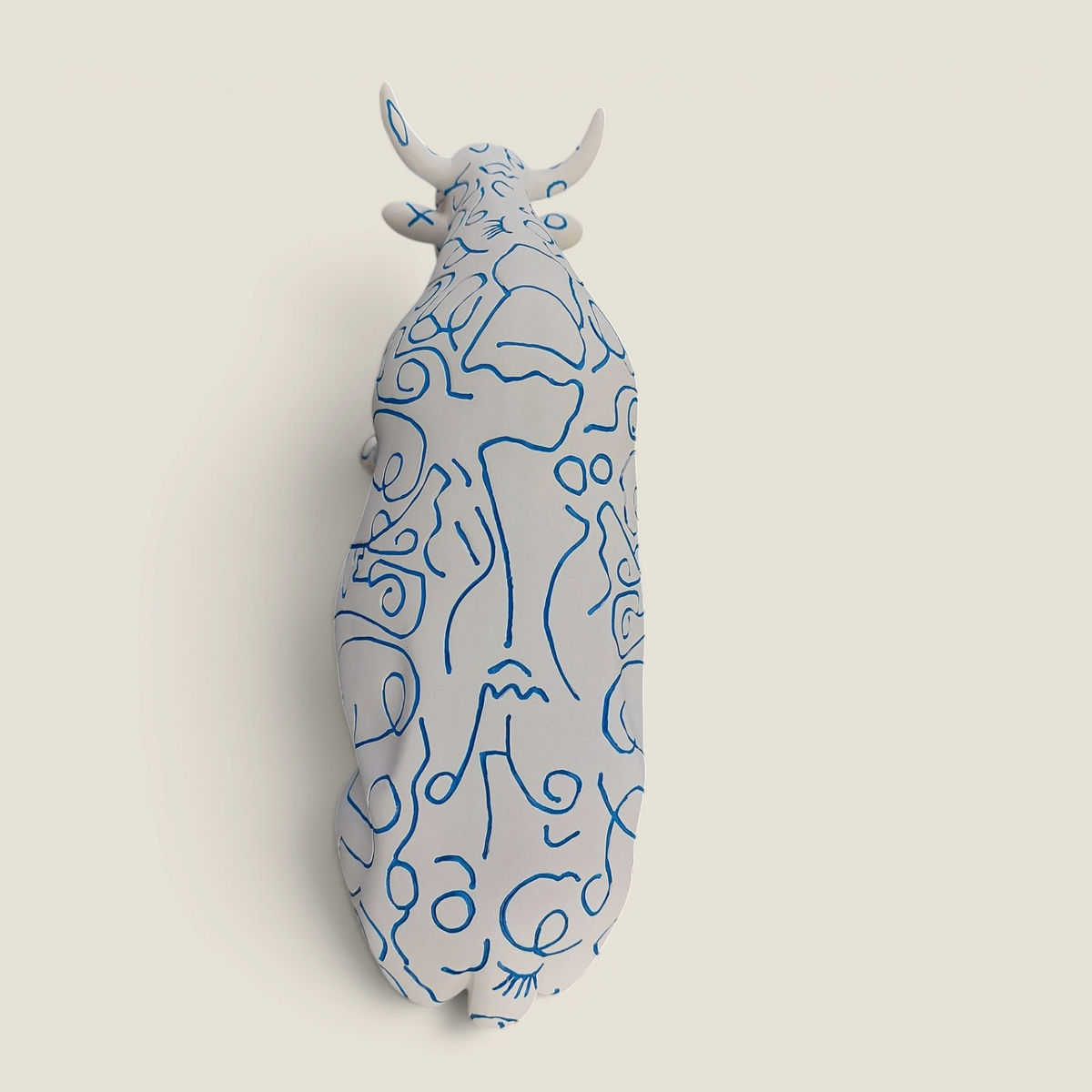 Figurine vache en résine Depuis des lustres, peinte à la main avec des motifs de visages bleus sur fond blanc.