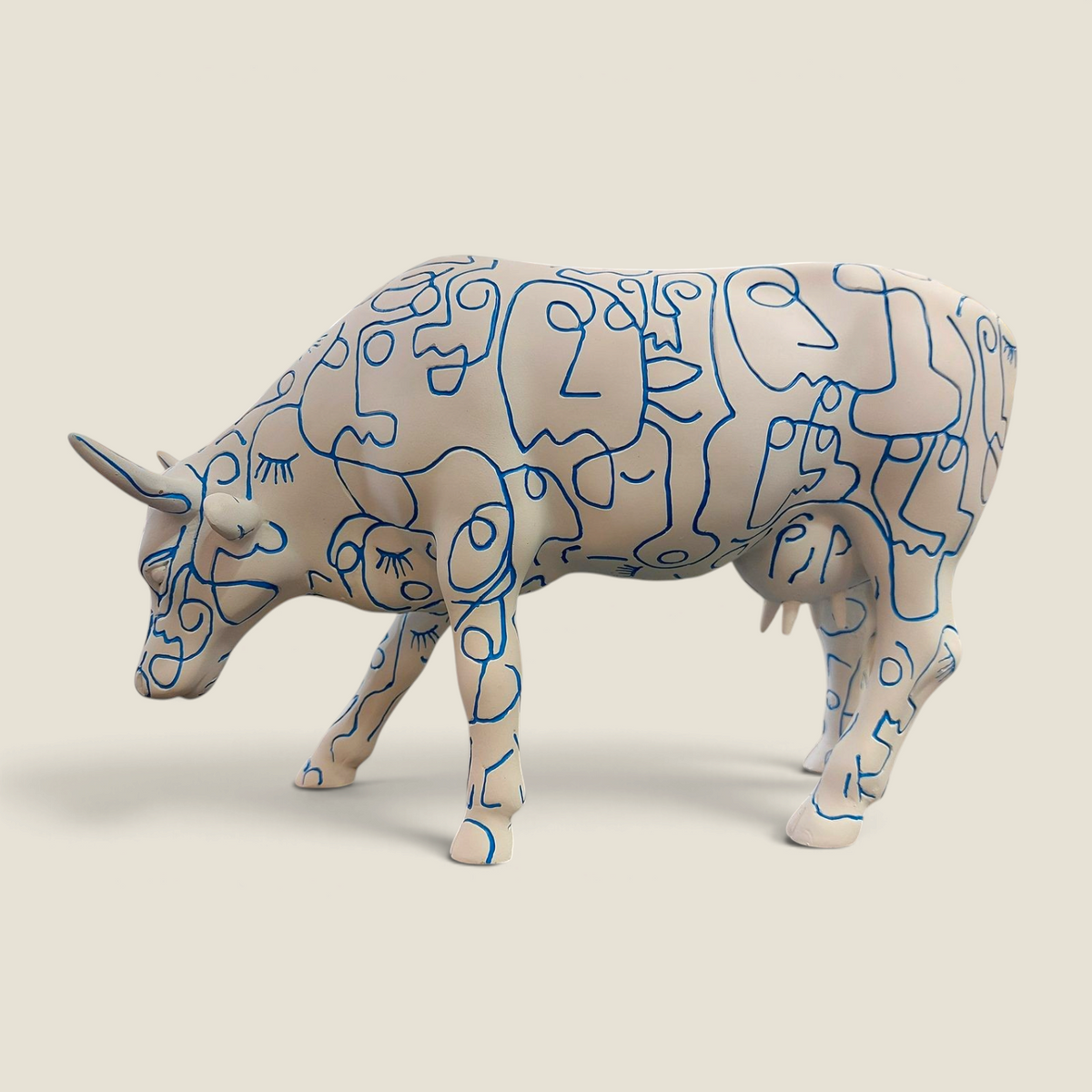Figurine vache en résine Depuis des lustres, peinte à la main avec des motifs de visages bleus sur fond blanc.