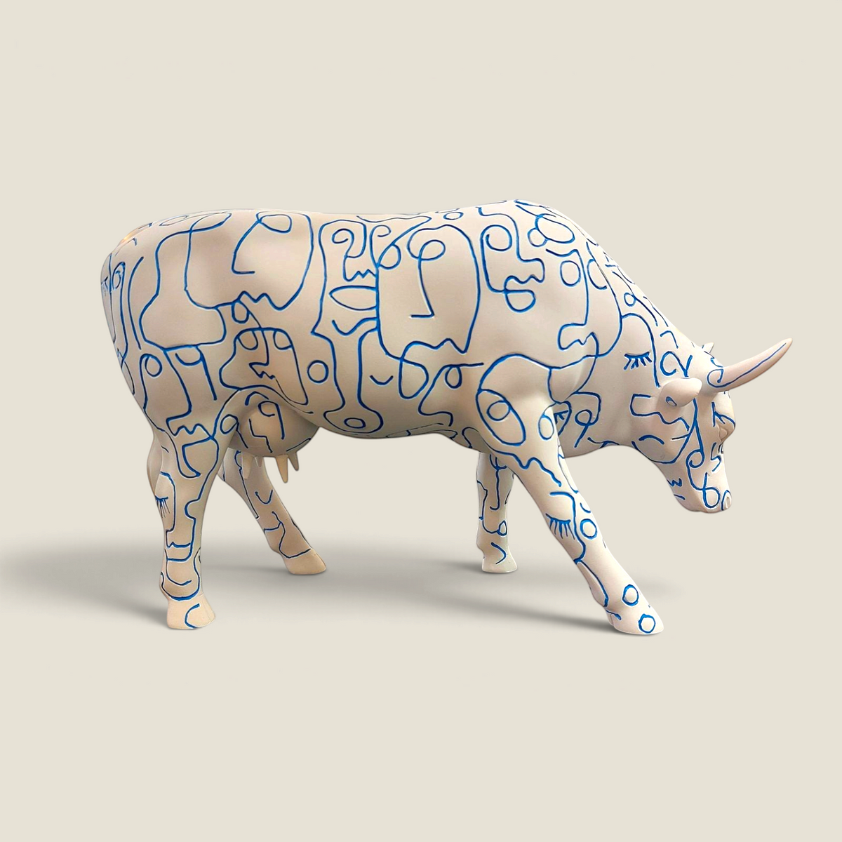 Figurine vache en résine Depuis des lustres, peinte à la main avec des motifs de visages bleus sur fond blanc.